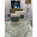 A scented candle in a glass jar on a clear glass tray with a box behind it.