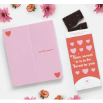 Pink greeting card and chocolate bar with small pink flowers around them