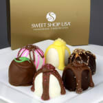 Assorted gourmet chocolate truffles on a white plate in front of a gold Sweet Shop USA box