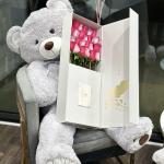 Teddy bear holding a box of pink roses