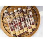 Five glass tubes filled with dried flower petals tied with twine on a wooden tray