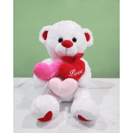 White teddy bear holding three heart pillows on a tabletop