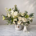 White floral arrangement in a white vase with a ribbon