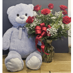 Red roses in a glass vase beside a large gray teddy bear