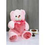 Pink teddy bear plush holding a darker pink heart pillow with a bow at its neck on a neutral backdrop