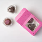 Pink box of heart-shaped chocolates with two loose chocolates nearby