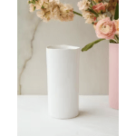 White cylindrical vase with pink and cream flowers nearby