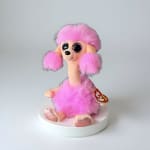 Pink plush poodle toy with glittery eyes sitting on a white base