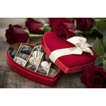 Red heart-shaped box of assorted chocolates with a white ribbon, surrounded by red roses