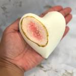 Hand holding a white heart-shaped decorative object with a pink and gold center