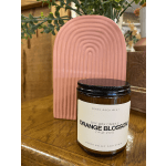 Orange blossom soy wax candle in an amber jar beside a pink arch decor piece