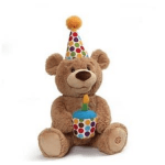Brown teddy bear with a polka dot party hat holding a plush cupcake with a candle.