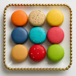 Square plate of nine colorful macarons arranged in a grid on a white background