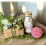 Gift box with ribbon, bath salt jar, and pink bath bomb on greenery