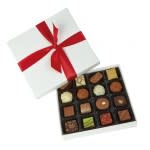 Gift box with a red ribbon beside an open box of assorted chocolates