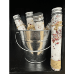 Four small glass jars filled with bath salts in a metal bucket