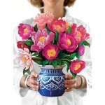 Person holding a blue patterned vase of pink flowers