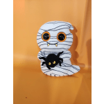 Plush mummy figure holding a small black spider on an orange background