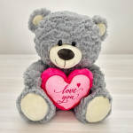 Gray teddy bear holding a pink heart that says love you