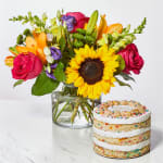 Mixed bouquet in a glass vase beside a layered cake