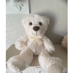 White teddy bear with a ribbon bow sitting on a shelf