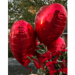 Red heart-shaped balloons above a bouquet of red roses