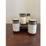 Group of jars of burnt caramel sauce on a wooden surface with one raised on a wood stand