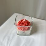 Coral rose-shaped candle in a square glass container