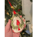 Hand holding a shell-shaped Christmas ornament with a cardinal design