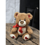 Plush teddy bear with a red ribbon sitting on a wooden surface