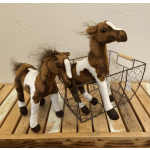 Two brown and white plush horses on a wooden surface, one standing and one in a wire basket