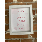 Framed sign with pink text reading "AND AT EVERY TABLE I'll save you a seat"