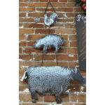 Metal wall art of a rooster, pig, and cow hanging on a brick wall