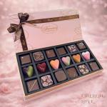 Box of assorted chocolates with a ribbon bow on a pink background