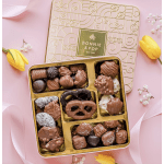 Box of assorted chocolates with yellow tulips on a pink background