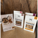Assorted Holm Made Toffee Co. Oregon hazelnut toffee boxes arranged on a woven mat.