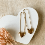 Two gold heart earrings on a white heart-shaped dish beside a peach flower