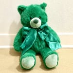 Green teddy bear with a satin bow sitting on the floor