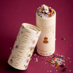 Two floral seasoning containers with dried petals and salt on a magenta background.