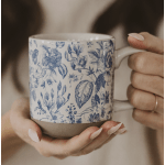 Hands holding a blue floral-patterned ceramic mug