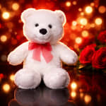 White teddy bear with a red ribbon beside red roses