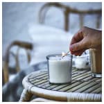 Hand lighting a white candle in a glass jar on a wicker table