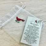 Small red bird ornament in a sheer pouch beside a memorial poem card