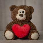 Brown teddy bear holding a red heart plush
