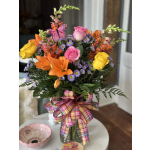Colorful bouquet of roses, lilies, and purple daisies in a glass vase with a plaid ribbon.