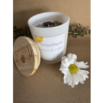 White candle in a glass jar with a wooden lid and a daisy flower beside it.