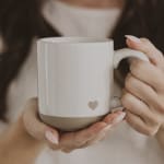 Hands holding a white ceramic mug with a small heart detail
