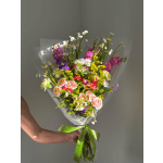 Handheld bouquet of pink, yellow, white, and purple flowers wrapped in clear paper