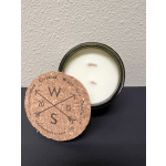 A white candle in a dark tin with a cork lid leaning in front
