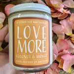 Jar candle labeled Love More surrounded by pink flower petals